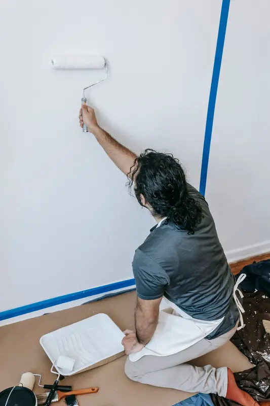 Een schilder rolt een witte muur, met blauw afplaklint langs de hoeken.