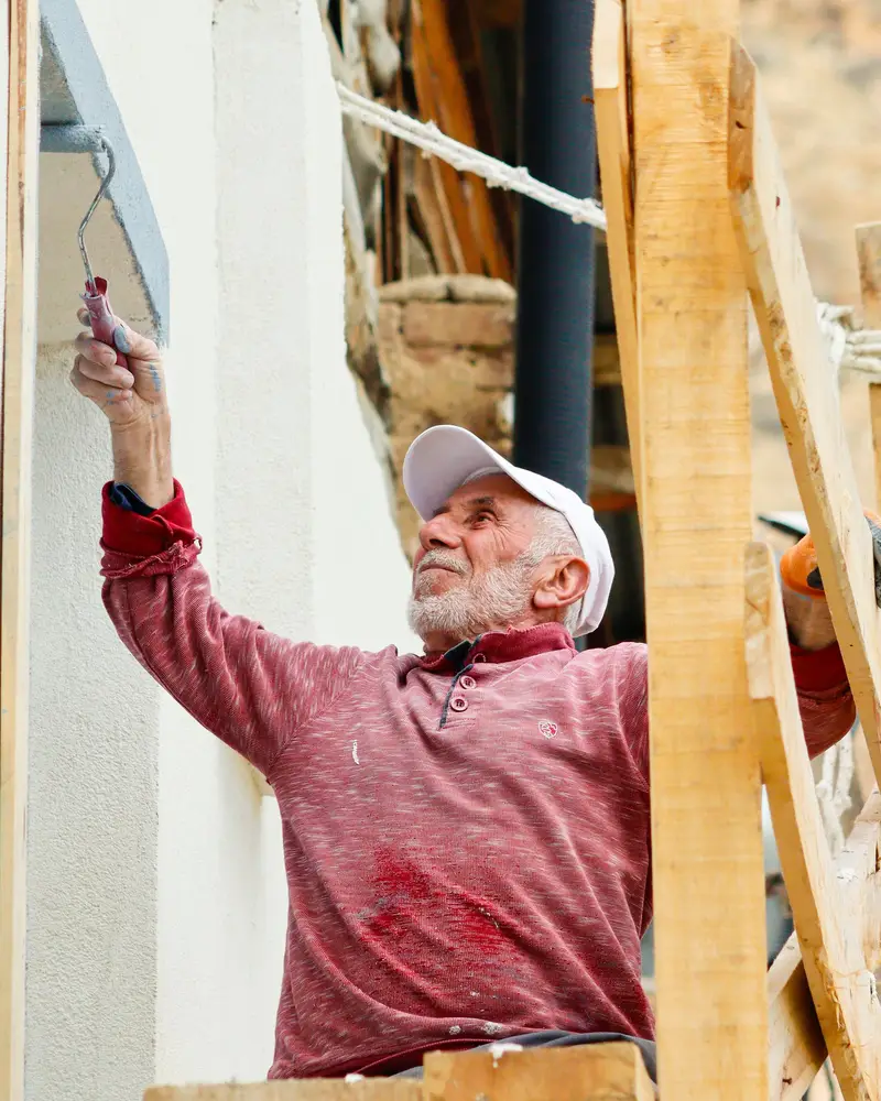 Een schilder op een stelling schildert een witte buitenmuur.