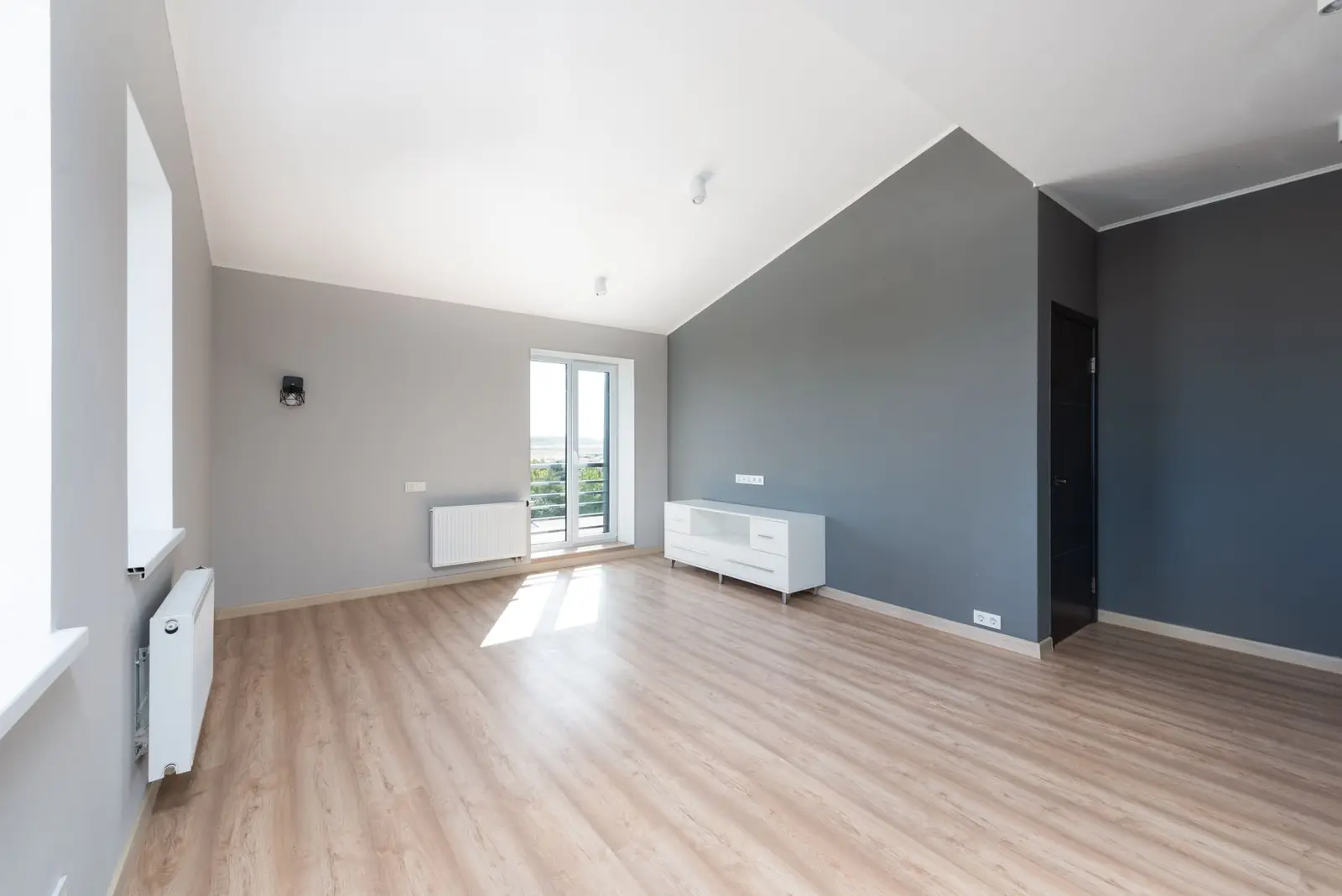 Lege nieuwbouwkamer met lichte muren en één donkergrijze accentmuur.